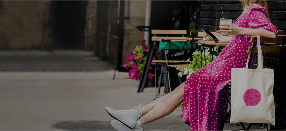 Femme en robe à pois utilisant une tablette en terrasse, avec un tote bag personnalisé