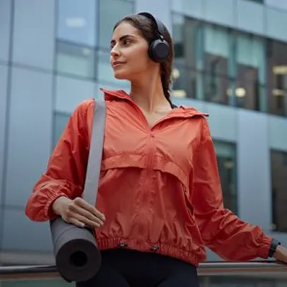 Femme en veste rouge avec écouteurs et rouleau de yoga en ville